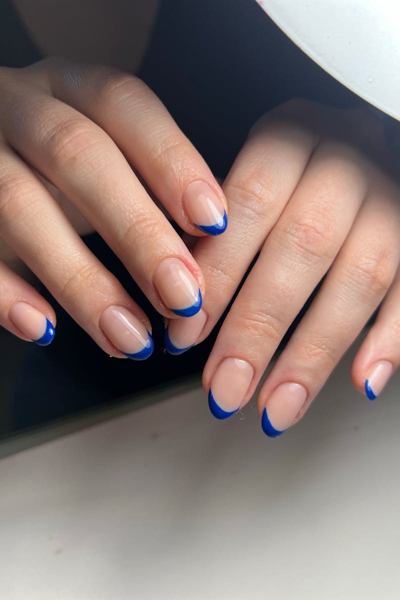 Close-up of a woman's hands with blue-tipped manicure under soft light.