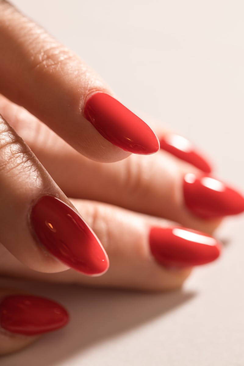 Close-up of elegantly manicured red acrylic nails illuminated by soft light.