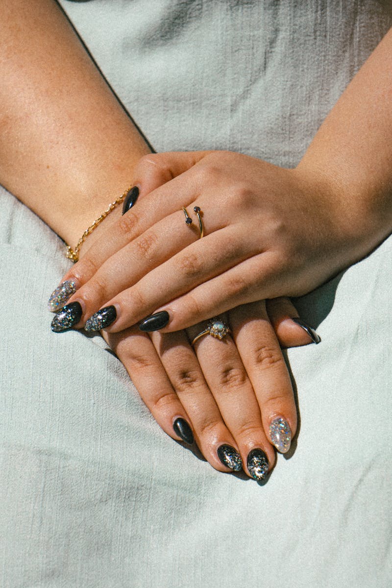 Close-up of hands with black and silver nail art wearing rings, bathed in sunlight.